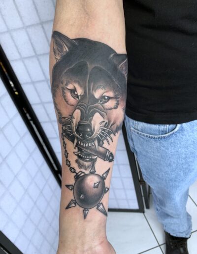 Neotradycjonalny tatuaż wilka z maczugą na przedramieniu wykonany w studiu Omerta Tattoo, Wrocław