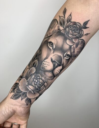Czarno-szary tatuaż lwicy z kwiatami na przedramieniu wykonany w studiu Omerta Tattoo, Wrocław