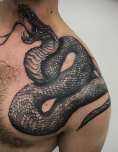 Czarno-biały, realistyczny tatuaż węża na obojczyku wykonany w studiu Omerta Tattoo, Wrocław