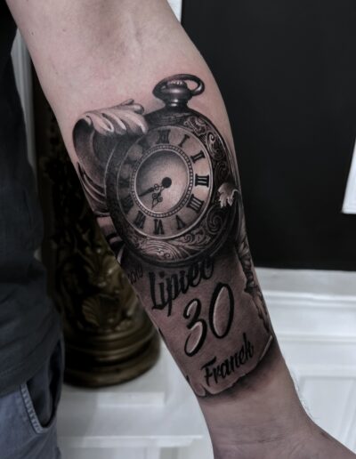 Realistyczny tatuaż zegara z datą i kalendarzem na przedramieniu wykonany w studiu Omerta Tattoo, Wrocław