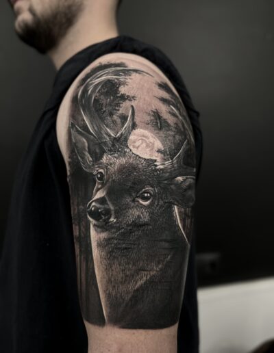 Realistyczny, czarno-szary tatuaż jelenia na ramieniu wykonany w studiu Omerta Tattoo, Wrocław