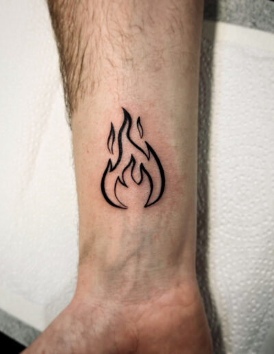 Minimalistyczny tatuaż płomienia - wlepka wykonany w studiu Omerta Tattoo, Wrocław