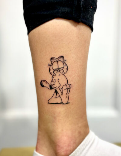 Minimalistyczny, konturowy tatuaż Garfield wykonany w studiu Omerta Tattoo, Wrocław